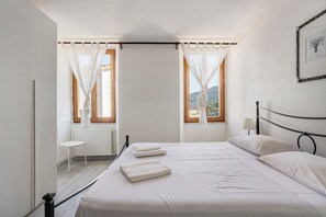A bedroom with a bed, two windows with curtains, a radiator, and a small table. - Holiday Home 'La ca Bela' with Sea View, Garden and Wi-Fi (portovenere la spezia)