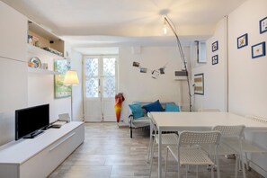 Ein modernes Wohnzimmer mit Fernseher, weißen Möbeln, einem Esstisch und einer blauen Couch.