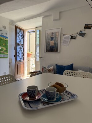 A dining area with a table set for two, a door leading outside, a wall with a framed picture, and a bulletin board with photos. - Holiday Home 'La ca Bela' with Sea View, Garden and Wi-Fi (portovenere la spezia)