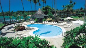 Zwembad van een resort met ligbedden, palmbomen en uitzicht op de oceaan.