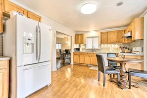 Una cocina con gabinetes de madera, un refrigerador blanco, una mesa de comedor con sillas y un horno empotrado.