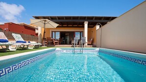 Ein Schwimmbecken mit gefliestem Rand, Liegestühlen und einer überdachten Terrasse.