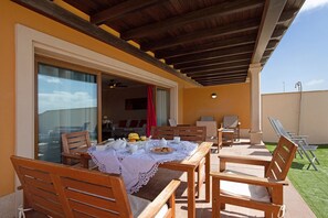 An outdoor patio with a table set for breakfast, wooden chairs, and a covered area with a view of the sky.