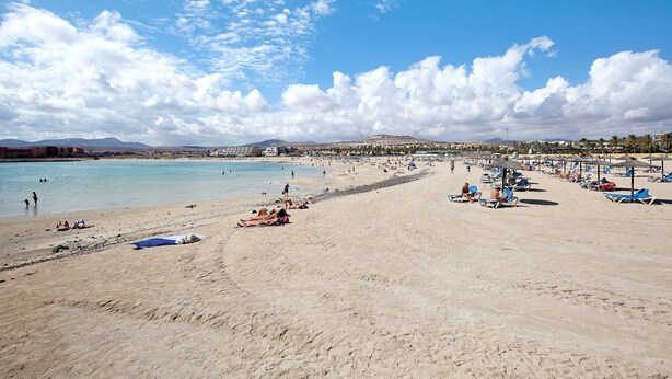 Ein Strand mit blauem Himmel, sandigem Ufer und einer fernen Bergkette.