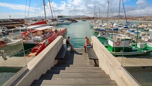 Ein Yachthafen mit vor Anker liegenden Booten, eine Holztreppe, die zum Wasser führt, und ein klarer Himmel.