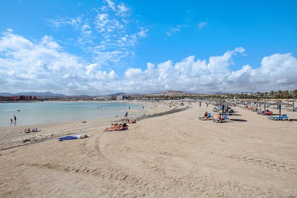 Une plage avec un ciel dégagé, une rive sablonneuse et une chaîne de montagnes à l’horizon.