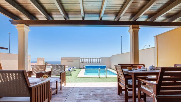 Eine Terrasse im Freien mit Holzmöbeln, einem Pool und Blick auf den Ozean.