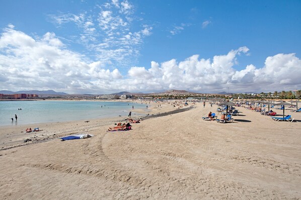 A beach with people sunbathing and swimming, umbrellas, and a clear sky.