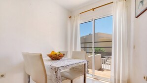 A balcony with a table and chairs, a basket with fruit, and a view of the outside.