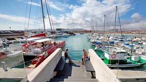A marina with boats docked, a wooden walkway, and a mountainous landscape in the background.
