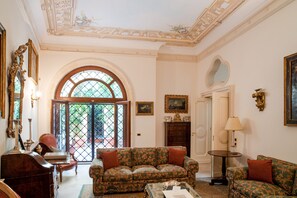 A room with a patterned sofa, a wooden cabinet, a round table, and a large arched window.