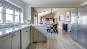 A modern kitchen with a central island, stainless steel appliances, and a dining area with a table and chairs. - Pen y Bryn -  a cottage that sleeps 10 guests  in 5 bedrooms (Pwllheli)