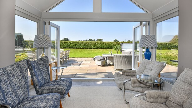 A sunlit conservatory with wicker furniture, a glass table, and a view of a well-maintained garden. - Pen y Bryn -  a cottage that sleeps 10 guests  in 5 bedrooms (Pwllheli)