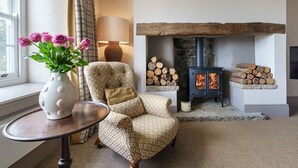 A cozy living room with a fireplace, a patterned armchair, a vase with flowers, and a lamp. - Pen y Bryn -  a cottage that sleeps 10 guests  in 5 bedrooms (Pwllheli)