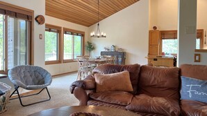 Ein geräumiges Wohnzimmer mit einem braunen Ledersofa, einem grauen Sessel und einer Holzbalkendecke.