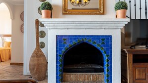 Une cheminée ornée de carreaux de mosaïque bleus, un miroir avec un cadre doré et deux plantes en pot posées sur le manteau de la cheminée.