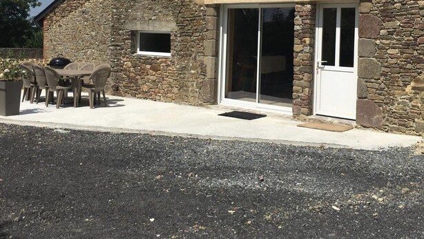 Un edificio con facciata in pietra, un'autorimessa e un patio con mobili da esterno.