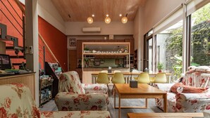 A cozy living room with floral-patterned furniture, a wooden dining table, and a kitchen in the background.