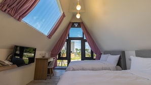 A bedroom with a large window, a desk with a chair, a bed, and a television.