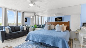 A modern hotel room with a large bed, a sofa, a desk, and a TV.