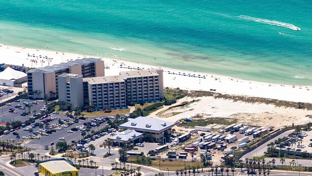An aerial view of a coastal hotel with multiple buildings, a parking lot, and a beach.