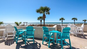 A beachside patio with turquoise Adirondack chairs and a view of the ocean.