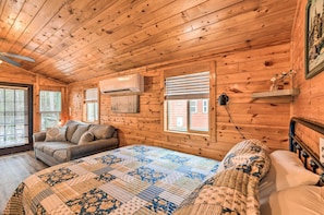 Une chambre confortable dans un chalet, avec un plafond en bois, un lit recouvert d’une courtepointe à motifs, un canapé avec des coussins et une fenêtre équipée de stores.