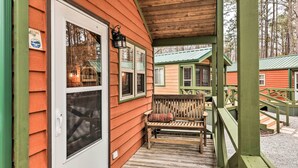 Une cabane en bois avec une véranda, un banc et une porte dotée d’une fenêtre.