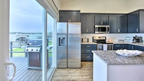 A modern kitchen with dark cabinets, stainless steel appliances, and a large window overlooking a deck.