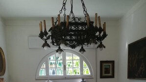 A dining area with a chandelier, a table with a fruit bowl, and a window with a view of greenery. - 3 Bedroom Villa in Massa (Massa)