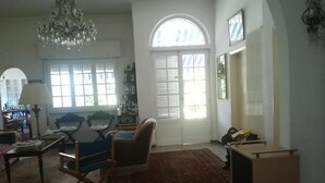 A spacious living room with a large window, a chandelier, and a wooden coffee table. - 3 Bedroom Villa in Massa (Massa)