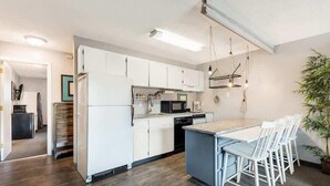 A modern kitchen with white cabinets, a central island, bar stools, and a hanging light fixture. - River View Condo- Edge of Downtown (Bend)