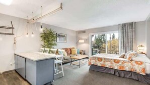 A modern hotel room with a kitchenette, a sofa, a bed, and a large window with a view of trees. - River View Condo- Edge of Downtown (Bend)