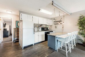 A modern kitchen with white cabinets, a granite countertop, and a bar area with white chairs. - River View Condo- Edge of Downtown (Bend)