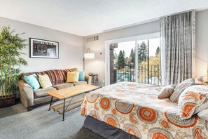 A modern bedroom with a large bed, a sofa, a small table, and a potted plant. - River View Condo- Edge of Downtown (Bend)