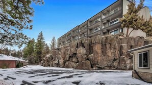 A multi-story building with balconies, situated next to a rocky cliff. - River View Condo- Edge of Downtown (Bend)