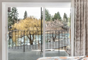 A room with a large sliding glass door leading to an outdoor area with a metal railing, a view of trees, and a river. - River View Condo- Edge of Downtown (Bend)