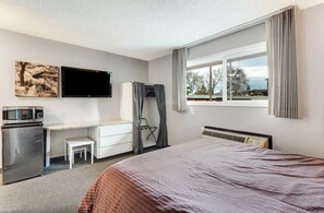 A hotel room with a bed, a desk, a television, a microwave, and a view of the outdoors. - River View Condo- Edge of Downtown (Bend)