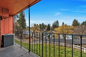 A balcony with a view of a river, trees, and a small building across the water. - River View Condo- Edge of Downtown (Bend)
