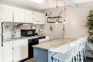 A kitchen with white cabinets, a granite countertop, a coffee maker, and a hanging light fixture. - River View Condo- Edge of Downtown (Bend)