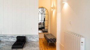 A modern interior with a marble floor, a black tray, a tufted bench, a radiator, and a window with a metal grille. - SKY DE LOIOS - Charming apartment with balcony (Porto)