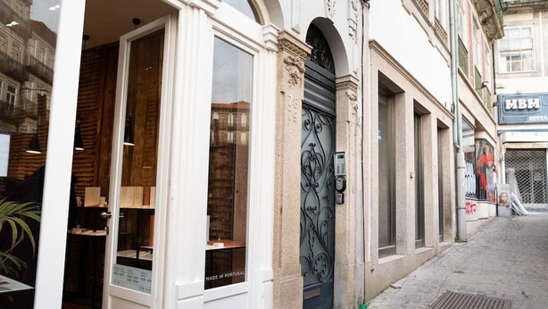 A storefront with a large glass window and a metal door, a brick wall, and a cobblestone street. - SKY DE LOIOS - Charming apartment with balcony (Porto)