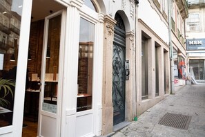 A storefront with a large glass window and a metal door, a brick wall, and a cobblestone street. - SKY DE LOIOS - Charming apartment with balcony (Porto)