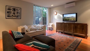 A living room with a sofa, a television, a wooden cabinet, and a large window. -  Emanjay: Walk to Beach, Million Dollar Bay Views! Mineral Spa (Mount Martha)