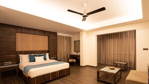 Ein Hotelzimmer mit einem großen Bett, einem Schreibtisch, einem Sessel, einem Couchtisch und einem Deckenventilator.