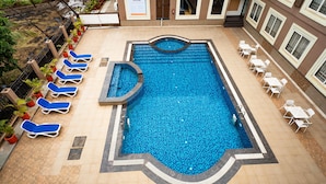 Ein Swimmingpool mit blauen Fliesen, umgeben von Liegestühlen und weißen Tischen.