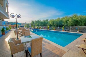 Zona de piscina con una mesa y sillas, rodeada de plantas en macetas y una valla.