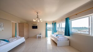 A modern hotel room with a bed, a sofa, a small table, and a view of the city. - The Senses Tsilivi Hotel (Zakynthos)