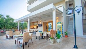 An outdoor cafe area with tables and chairs, a staircase, and a storefront with a sign. - The Senses Tsilivi Hotel (Zakynthos)