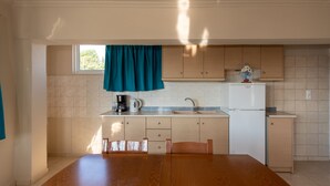 A kitchen with a wooden table, cabinets, a sink, and a window with curtains. - The Senses Tsilivi Hotel (Zakynthos)